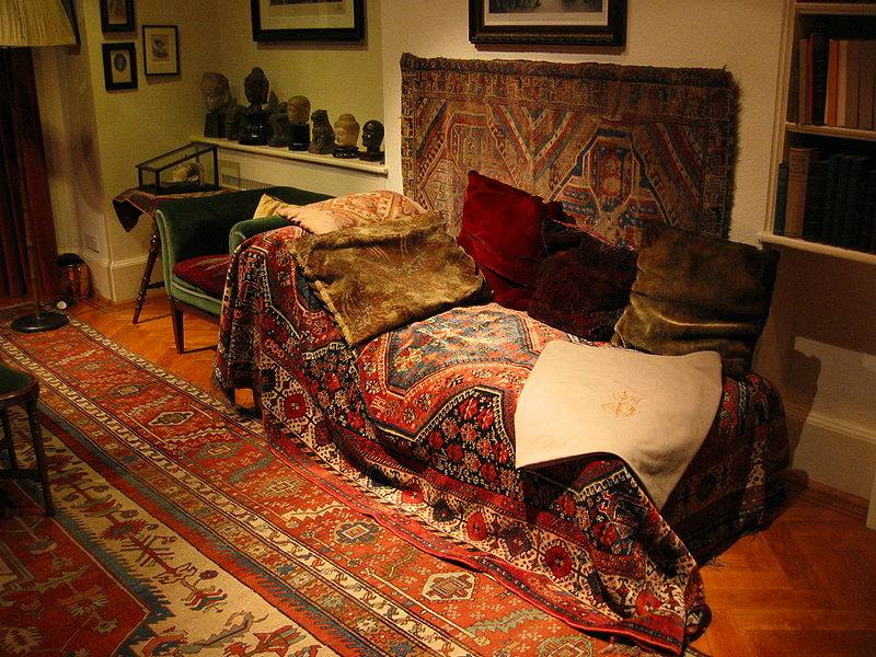 kanapa pokryta ornamentalnym czerwonym dywanem i poduchami
